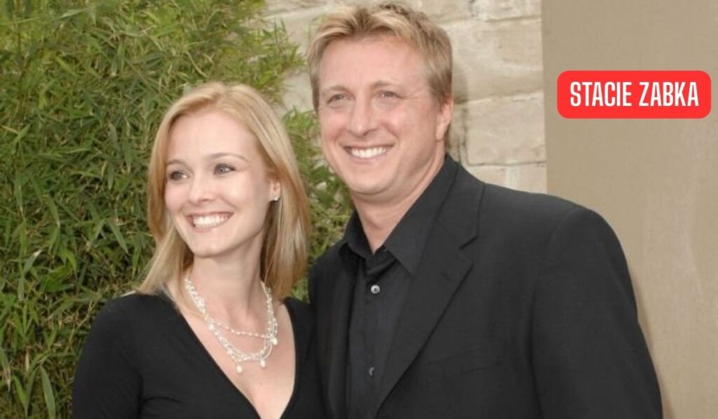 Stacie Zabka smiling alongside her husband at a public event, both dressed in elegant black outfits.
